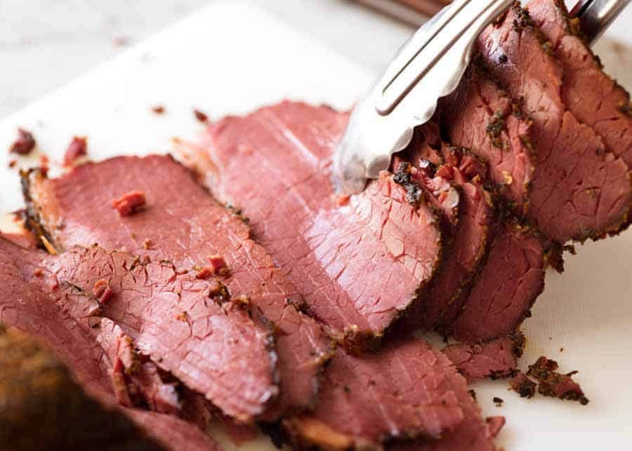 Easy homemade pastrami slices being picked up by tongs, ready to pile onto sandwiches