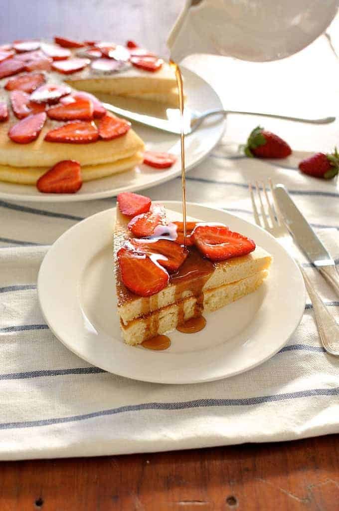 Maple syrup being poured over giant pancake slice