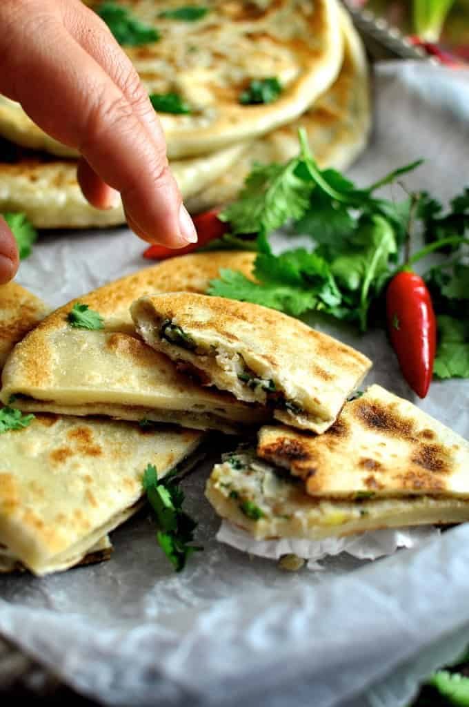 Hand reaching in to take a pice of Aloo Paratha (Indian Potato Stuffed Flatbreads) filled with mashed potato and spiced beef.