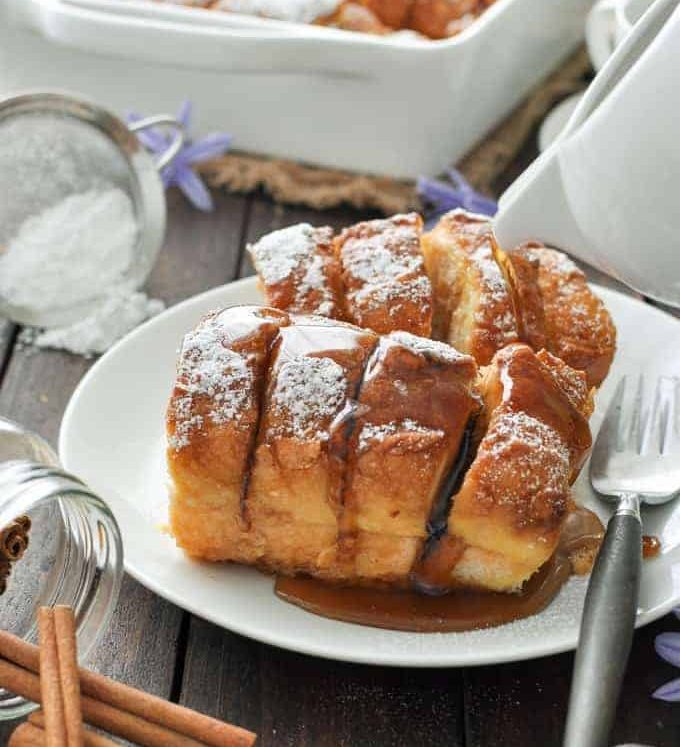 Hasselback Baked French Toast on a white plate, dusted with icing sugar and drizzled with maple syrup.