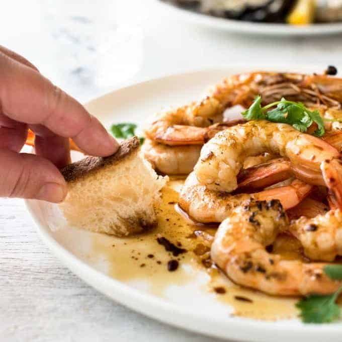 Bread being used to mop up the sauce on a plate of Asian Grilled Shrimp.