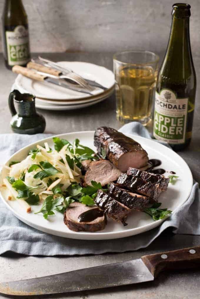 A plate of Apple Cider Glazed Pork Tenderloin with apple salad and cutlery