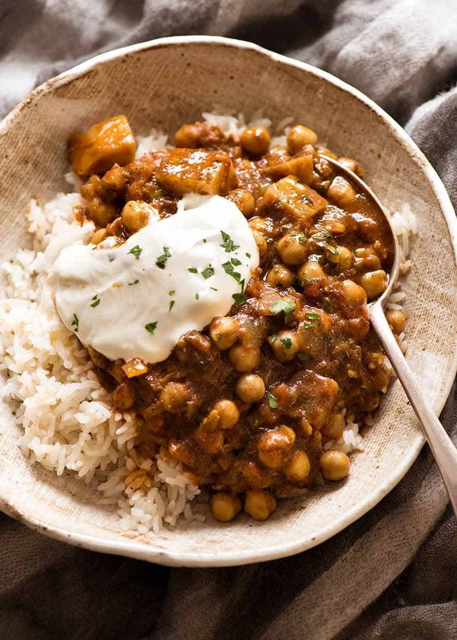 Photo of Chickpea Curry (Chana Aloo) in a bowl over coconut rice with a dollop of yogurt in a rustic bowl, ready to be eaten