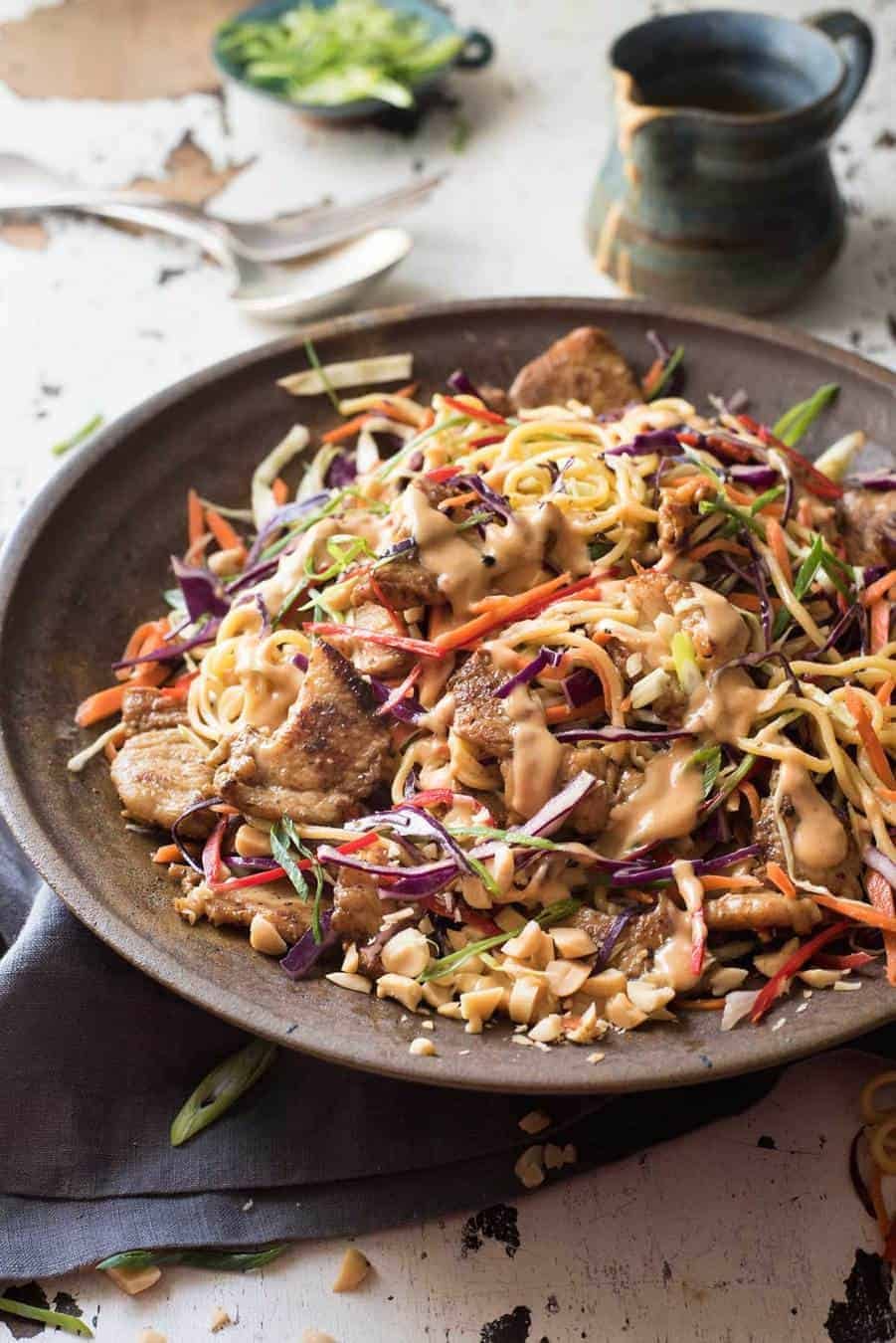 Satay Chicken Noodle Salad drizzled with peanut dressing in a rustic dark brown bowl.