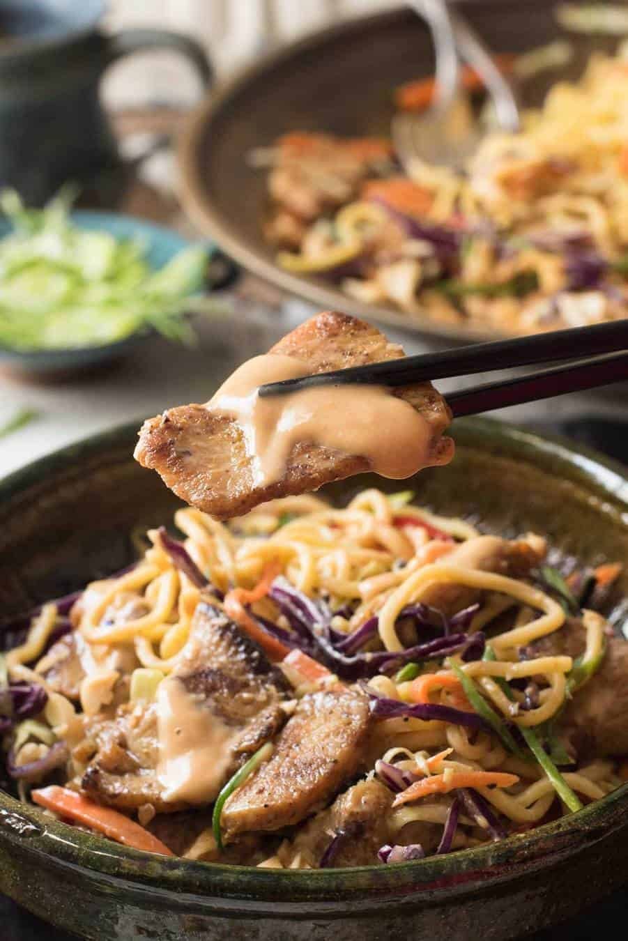 Close up of a piece of chicken drizzled with peanut dressing from a Satay Chicken Noodle Salad.