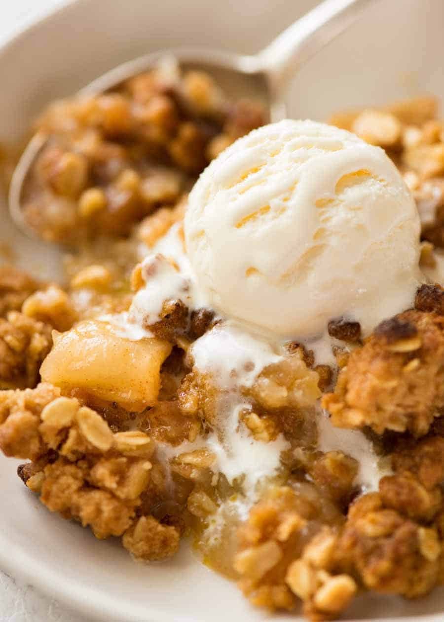 Close up of Apple Crumble in a rustic white bowl with a scoop of vanilla ice cream, ready to be eaten