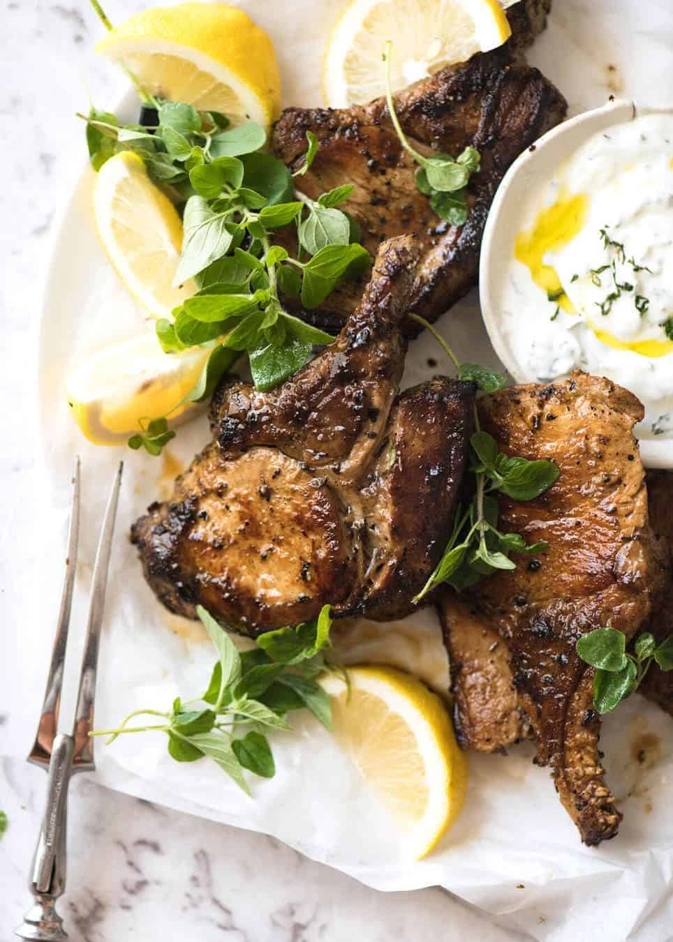 Lemon Garlic Marinated Grilled Pork Chops on a white plate with wedges of lemon and garnished with fresh oregano.