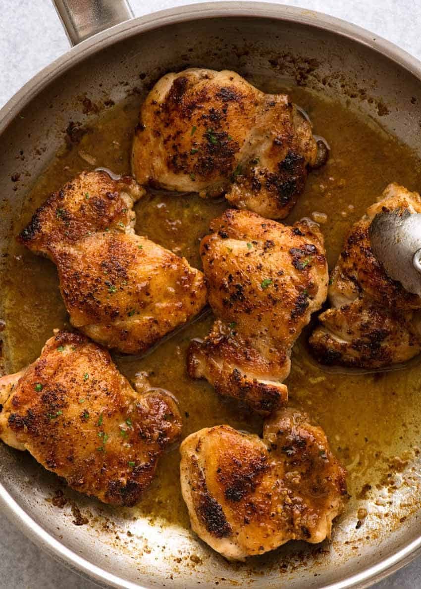 Overhead photo of Crispy Garlic Chicken Thighs in a silver pan with garlic butter sauce, fresh off the stove.