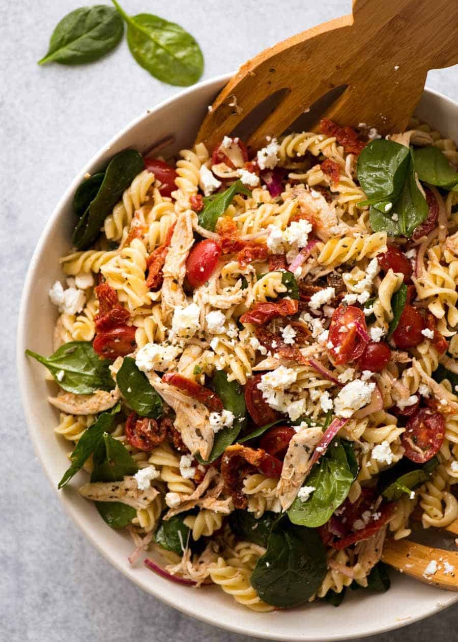 Overhead photo of Pasta Salad with Chicken and Sun Dried Tomato in a white bowl with salad servers, ready to be served