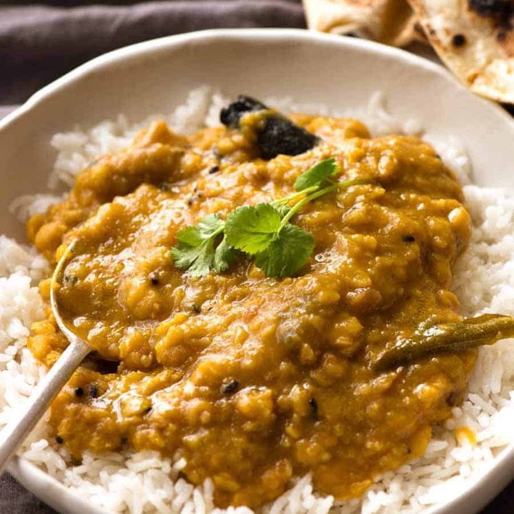 Homemade India lentil curry (Dal) served over rice in a rustic white bowl, ready to be eaten.