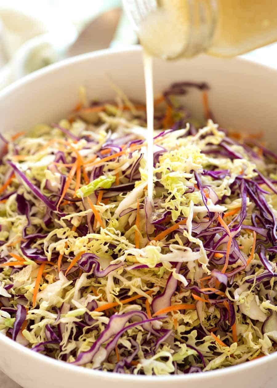 Vinaigrette being poured over Everyday Cabbage Salad in a white bowl