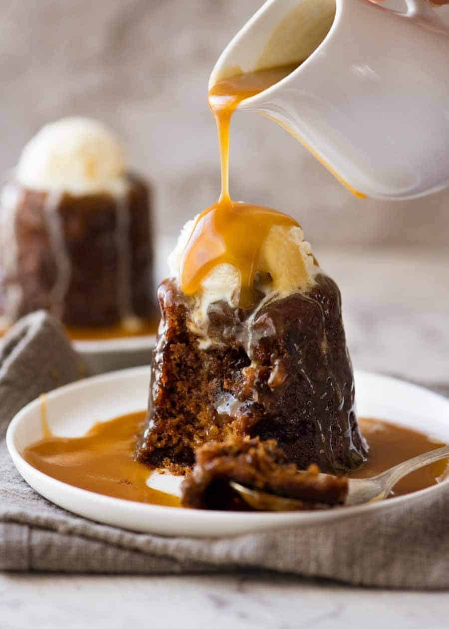 Butterscotch Sauce being poured over Sticky Toffee Pudding on a white plate, ready to be eaten