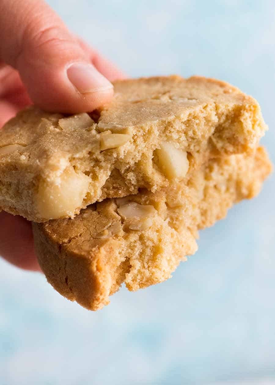 Hand holding White Chocolate Macadamia Nut Cookies broken in half to show inside