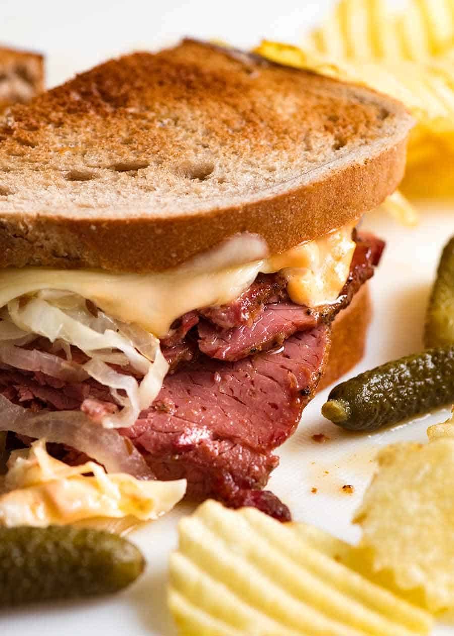 Reuben Sandwich loaded with homemade pastrami, easy quick sauerkraut, Russian Dressing, Swiss cheese on rye bread, ready to be eaten. Katz's deli copycat recipe.