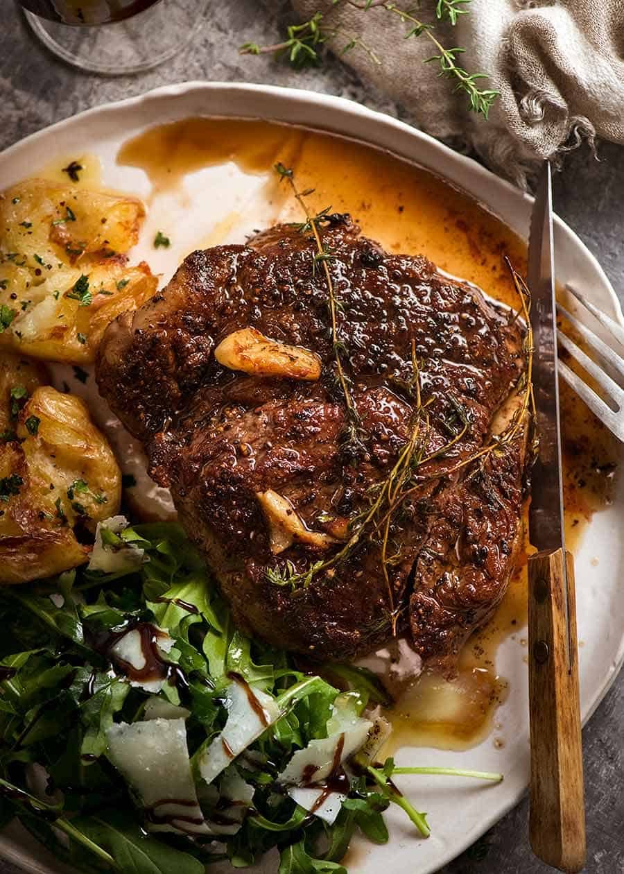 Pan Seared Steak with garlic butter sauce on a plate with a side of crispy smashed potatoes and rocket salad
