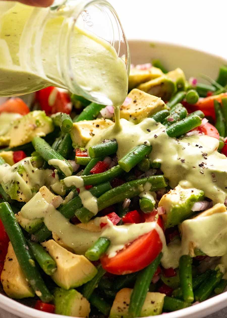 Pouring avocado dressing over Green Bean Avocado Salad with Avocado Dressing