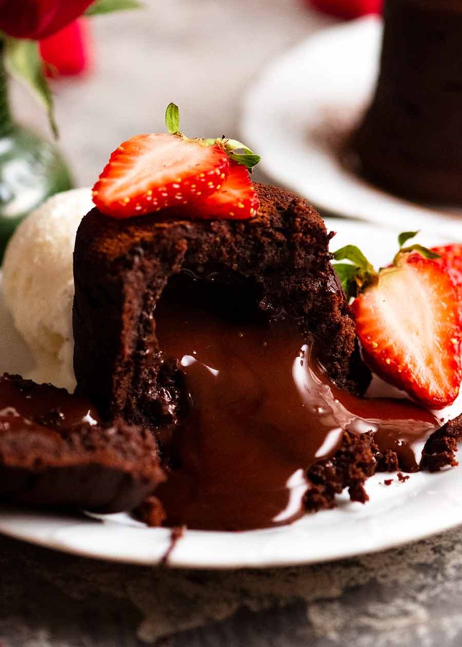 Close up of Molten Chocolate Cake with chocolate lava pouring out, decorated with strawberries and a scoop of ice cream