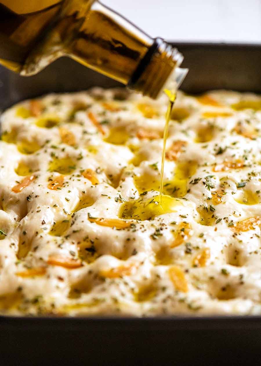 Drizzling olive oil over focaccia dough, ready to be baked